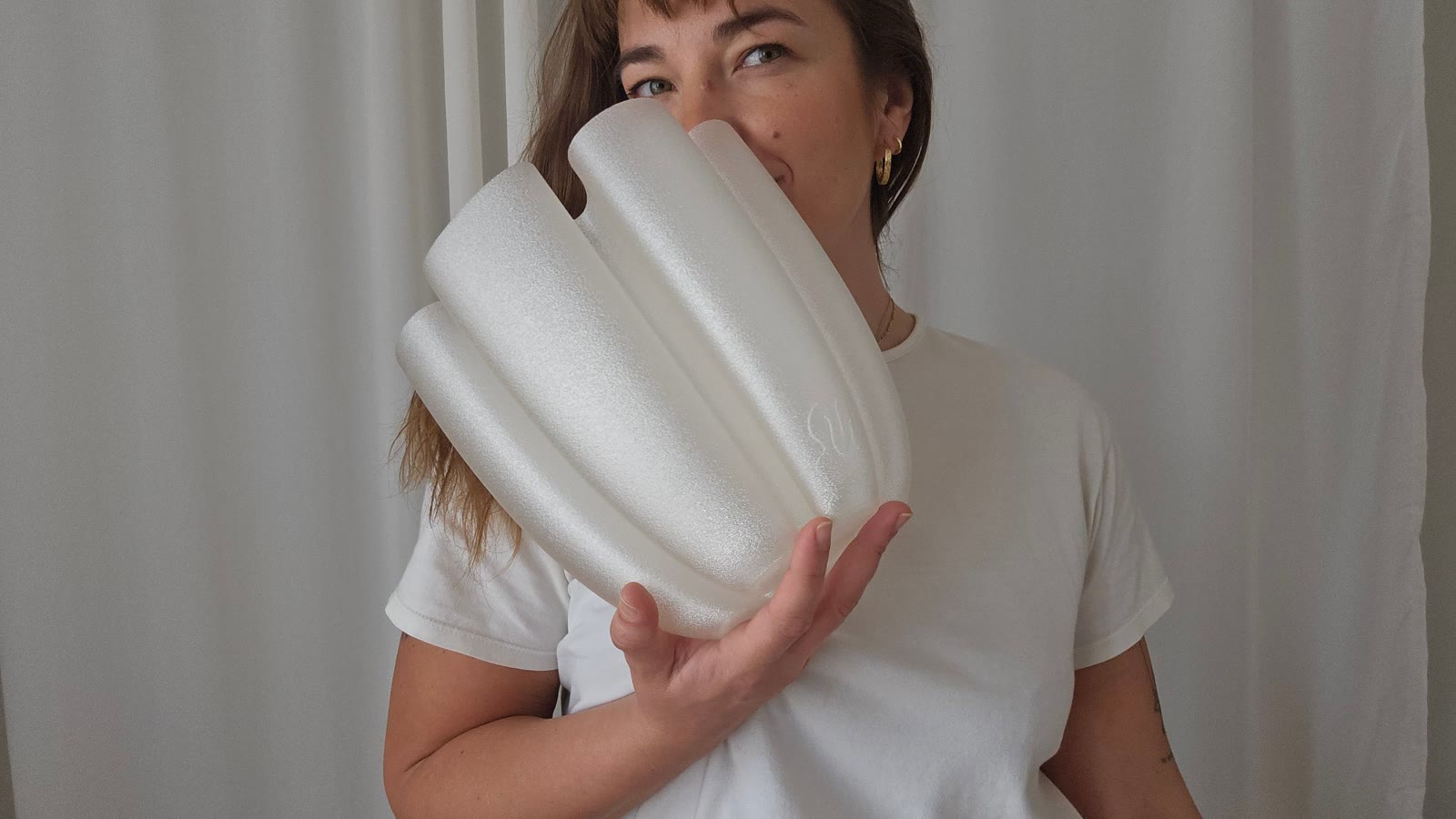 Aleksandra peeking out from behind a white fluted lamp she holds up to her face