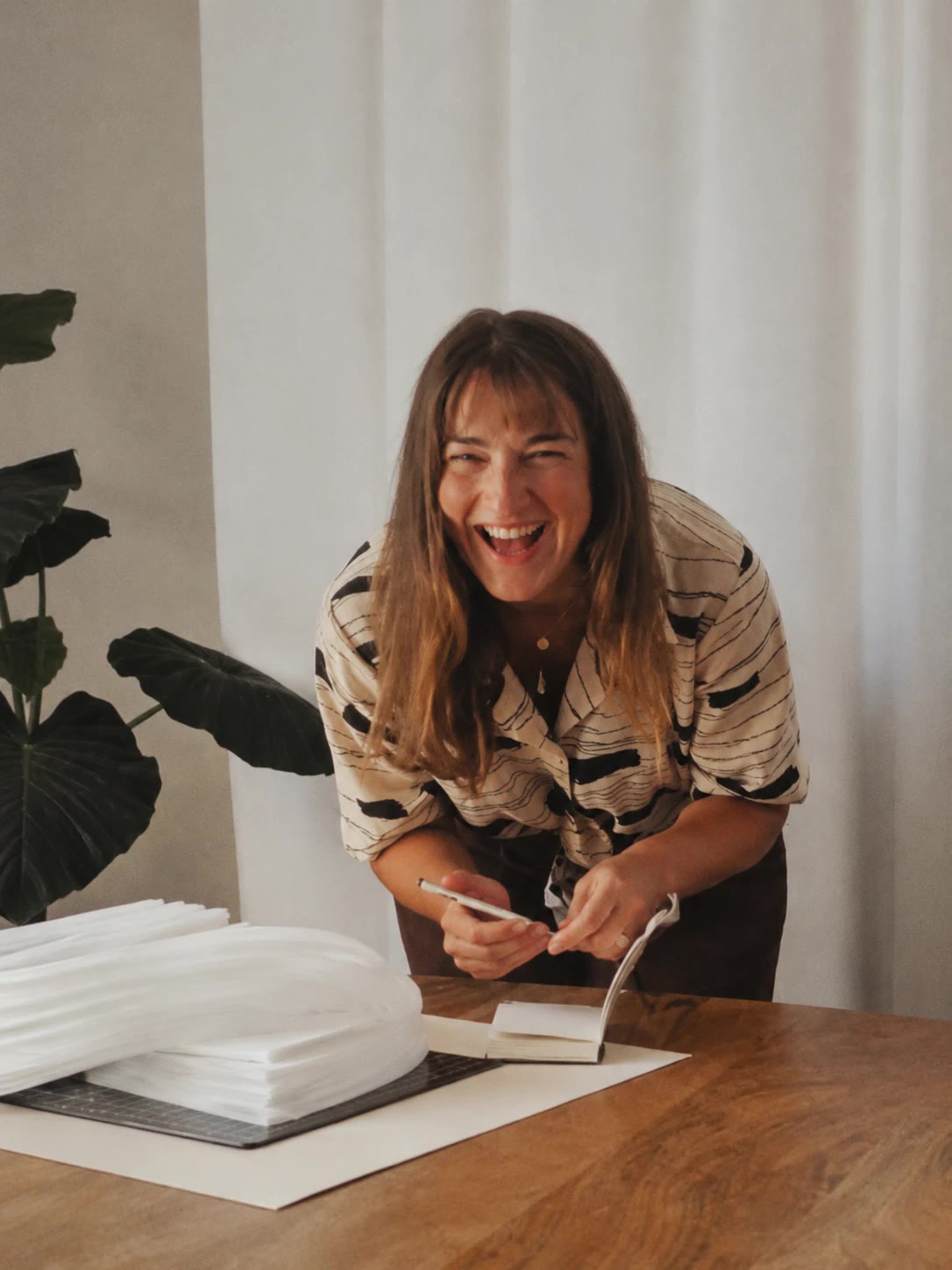 Aleksandra laughing as she leans over her studio table with a notebook