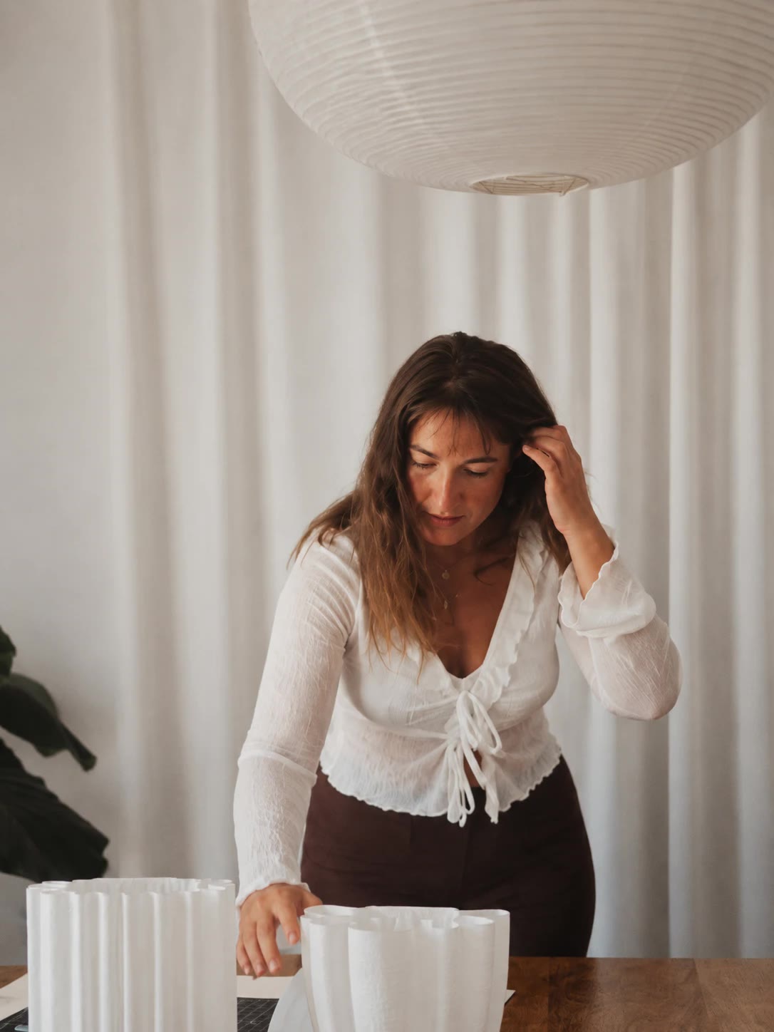 Aleksandra arranging two fluted lamp shades on her studio table under a paper lantern